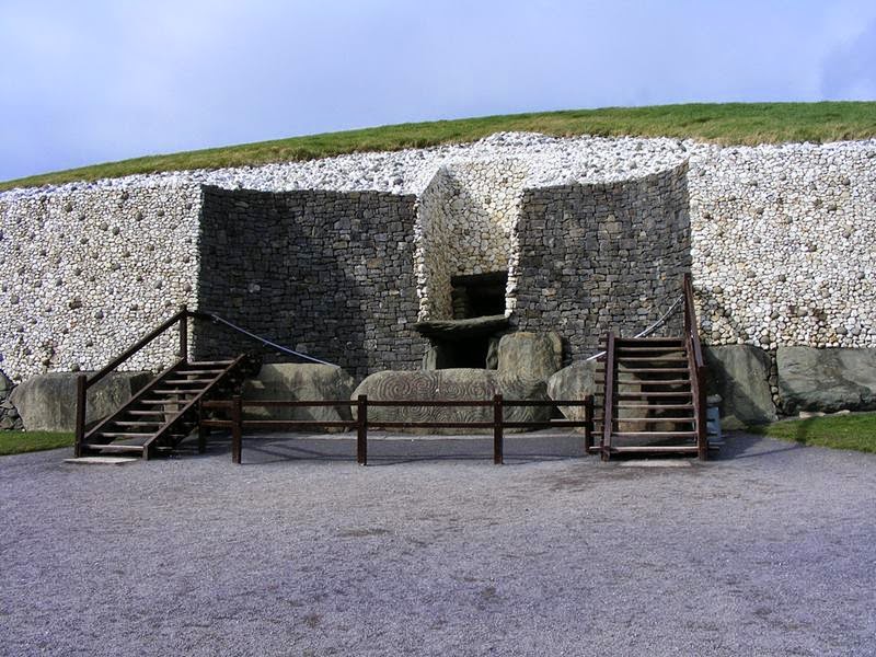 Entrance to Newgrange. The original entrance was "cut away" when the wall was reconstructed to provide better access (and stop people climbing over the stone that originally blocked the entrance way). The rebuilt wall is faced in the original white quartz with darker river stones dotted about, with the cut away section in the darker stone. The "window box" that lets light into the mound on the Winter Solstice is above the shelf type structure, which sits above the entrance itself.