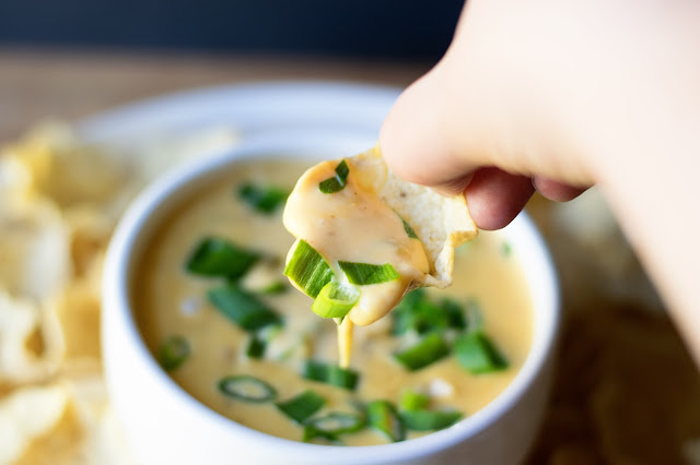 A chip dipping the queso out of a bowl.  