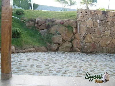 Detalhe do acabamento do canto do muro de pedra faceado e no início do talude o muro de pedra sem cimento com nichos para colocação de plantas com o piso de pedra bruta.