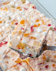 Frozen fruit salad is a blast from the past. This vintage recipe is a cool and delicious way to eat your fruit. It is at home at all of our holiday meals, but would also be a fun summer side dish! first piece of frozen fruit salad being lifted out of pan fresh from the freezer