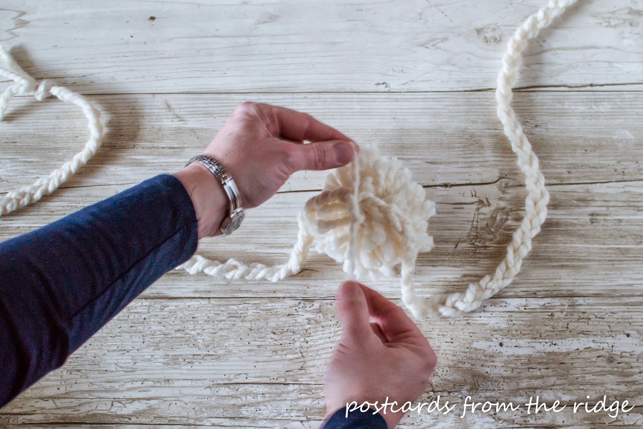 tying yarn pom pom to braided strand of yarn