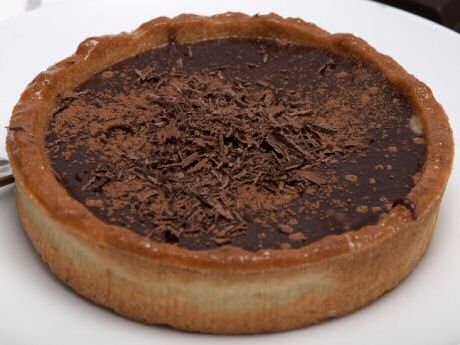 Makkelijke chocoladetaart met cacaopoeder in de blind gebakken taartkorst, gevuld met ganache en afgewerkt met cacaopoeder en geraspte chocolade