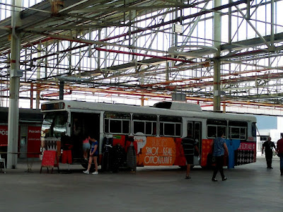 Under the roof of the building is parked a commuter bus decked out as a clothing shop.