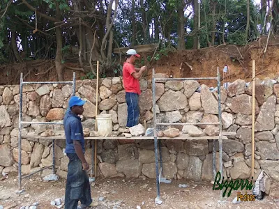 Execução do muro de pedra rústica com pedra do tipo moledo na face do muro e na parte de trás, no enchimento, a pedra rachão. Muro de pedra com os pilares de ferro armado com a cinta de ferro armada a cada 1,50 m de altura.