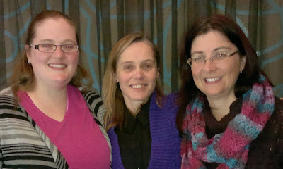 Michelle, Jodie and Adrienne. Michelle has a vivid pink top with grey and black striped knitted jacket, Jodie has a black shirt with the purple Belcarra cardigan and Adrienne has a dark plum coloured jumper with a variegated scarf in plumps, pinks, mauves and blues which she crocheted herself.
