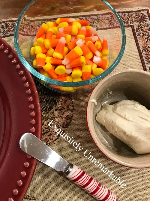 A bowl of candy corn, frosting, a small knife on a rooster placemat