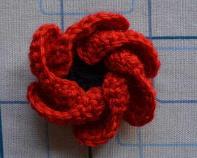 "Hope Bloom" poppy on ironing board. Red petals are curled inwards, covering some of the black centre.