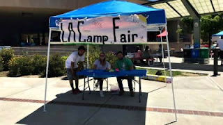 L.A. Camp Fair volunteers and representatives sitting under a blue canopy at the Camp Fair sign-in registration booth at AC Stelle Middle School, Calabasas.