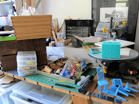 A work bench covered with various one-twelfth scale modern miniatures, accessories and tools.