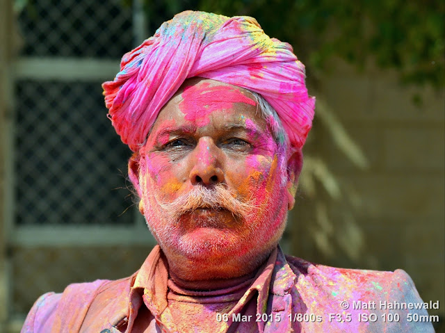 Closeup street portrait (outdoor headshot, full-face view) of an Indian "Holi man", dusted heavily with synthetic colour powder of unknown toxicity; Holi Festival 2015, Jaisalmer, Rajasthan, India. Matt Hahnewald Photography; Facing the World; closeup; street portrait; headshot; outdoor; world; cultures; cultural; one person; character; people; male; adult; ethnic; local; traditional; human; face; eyes; Asia; India; Rajasthan; Jaisalmer; eye contact; front view; en face; photography; consent; empathy; rapport; portrait; portraiture; ethnic portrait; travel portrait; travel destination; colour; colourful; 4 : 3 aspect ratio; horizontal; smiling; Nikon D3100; posed; Nikkor AF-S 50mm f/1.8G; Indian man; festival; Holi Festival; Festival of Colours; colour powder; turban; moustache