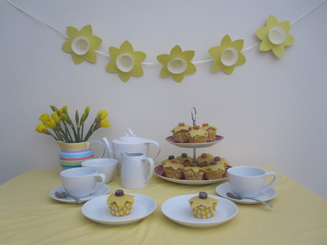 A table set for afternoon tea with cups and saucers, cupcakes on a stand, teapot and a jug filled with fresh daffodils