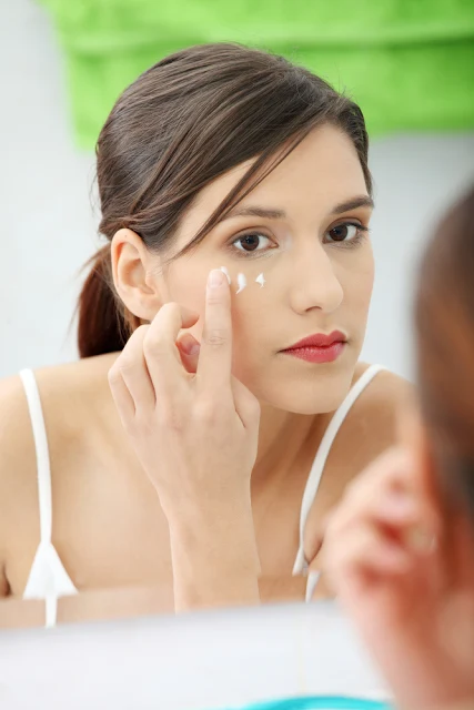 woman in mirror adding eye cream