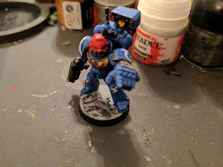 A Ultramarine's Space Marine Sargent pointing into the forground with an oversized hand. He has a bright red helmet