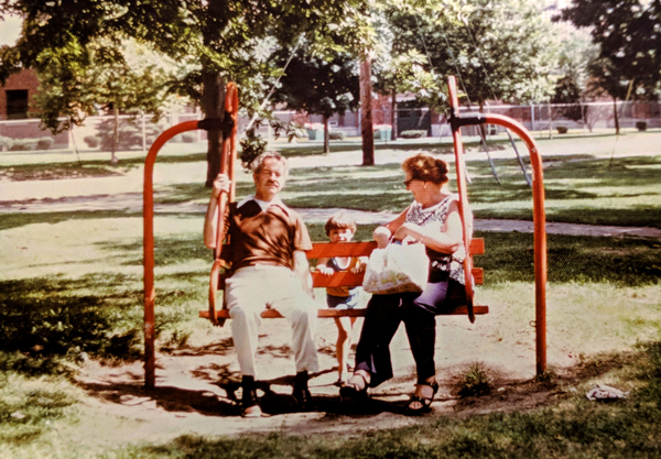 image of me as a tiny 4-year-old, at a park with my grandparents in the summertime, pushing them on a bench swing