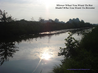 Mirroring & Modelling: how to change it to create a better life Sun and clouds refelcting in a strip of water surrounded by trees. With wording: Mirror what you want to see, Model who you want to become