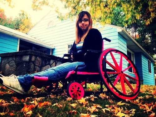 Young woman in a manual wheelchair that has been modified to "ride low", and with pink painted highlights