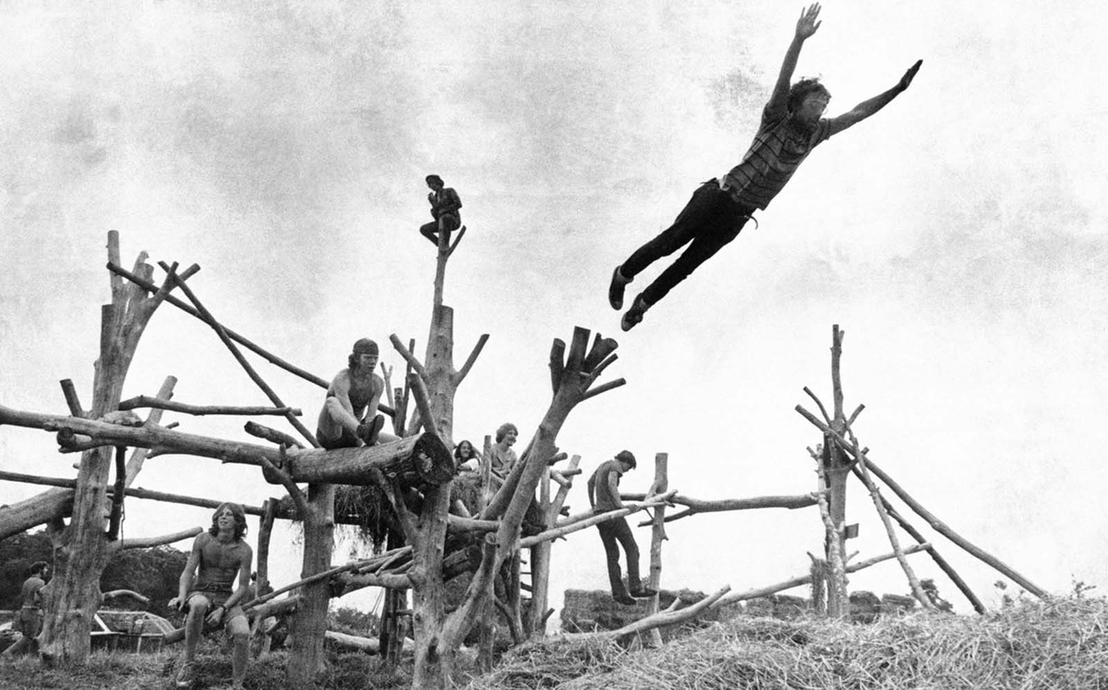Rock-music fans sit on a tree sculpture as one leaps midair onto a pile of hay during Woodstock on August 15, 1969.