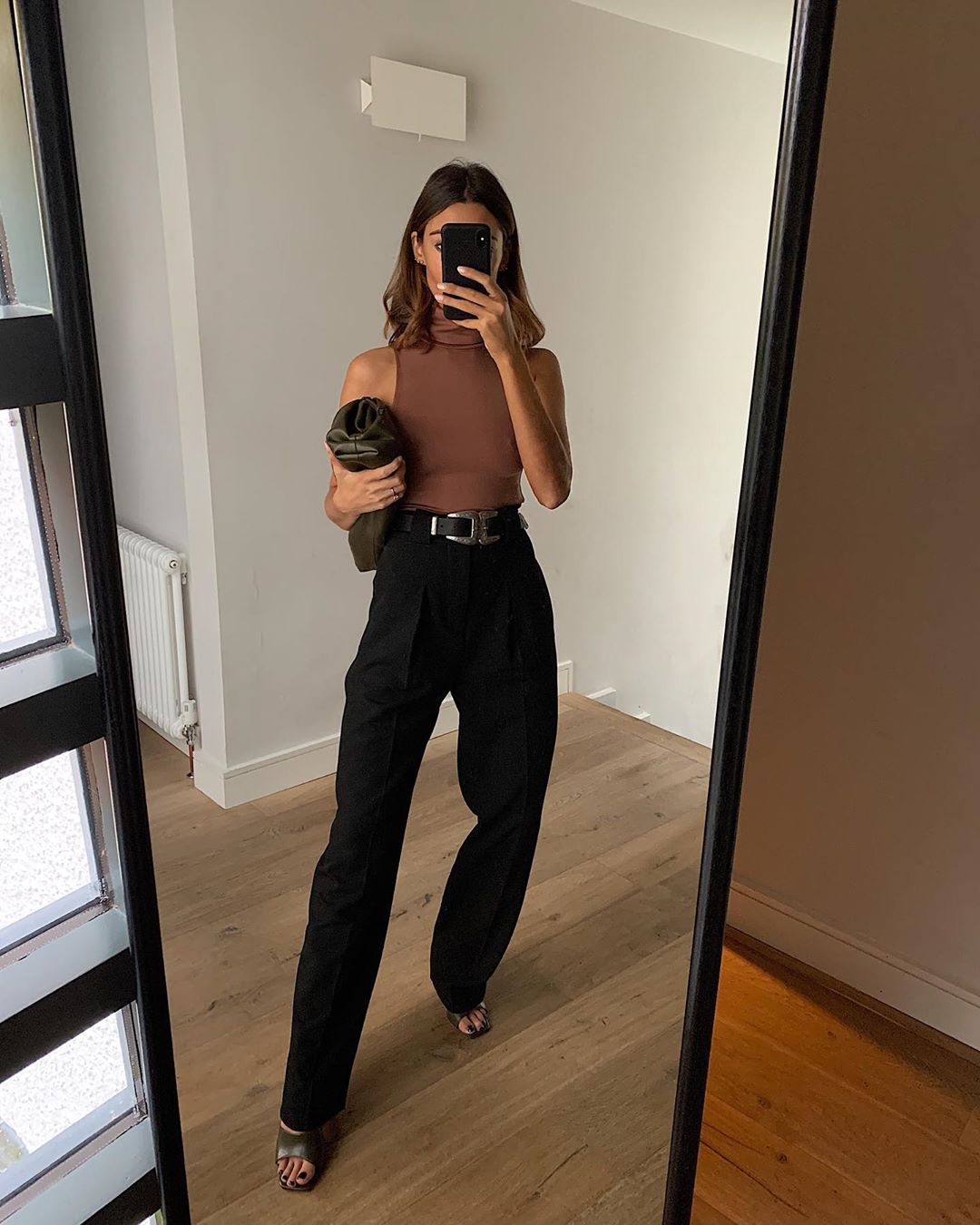 @smythsisters Instagram outfit idea — brown sleeveless turtleneck top, belt, high-waisted pants, black pouch clutch, and black mule heel sandals