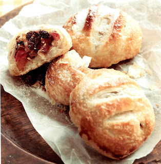 Luxury eccles cakes. Three pastries of mixed dried fruit in a puff pastry shell, one broken open