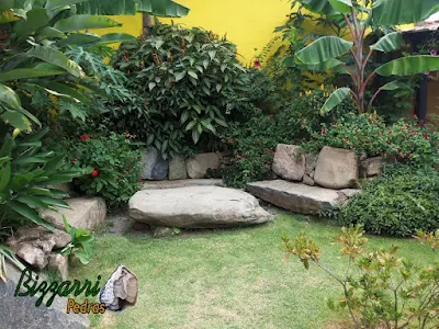 Banco de pedra no jardim, com pedra moledo, e a mesa de pedra com a execução do paisagismo natural.