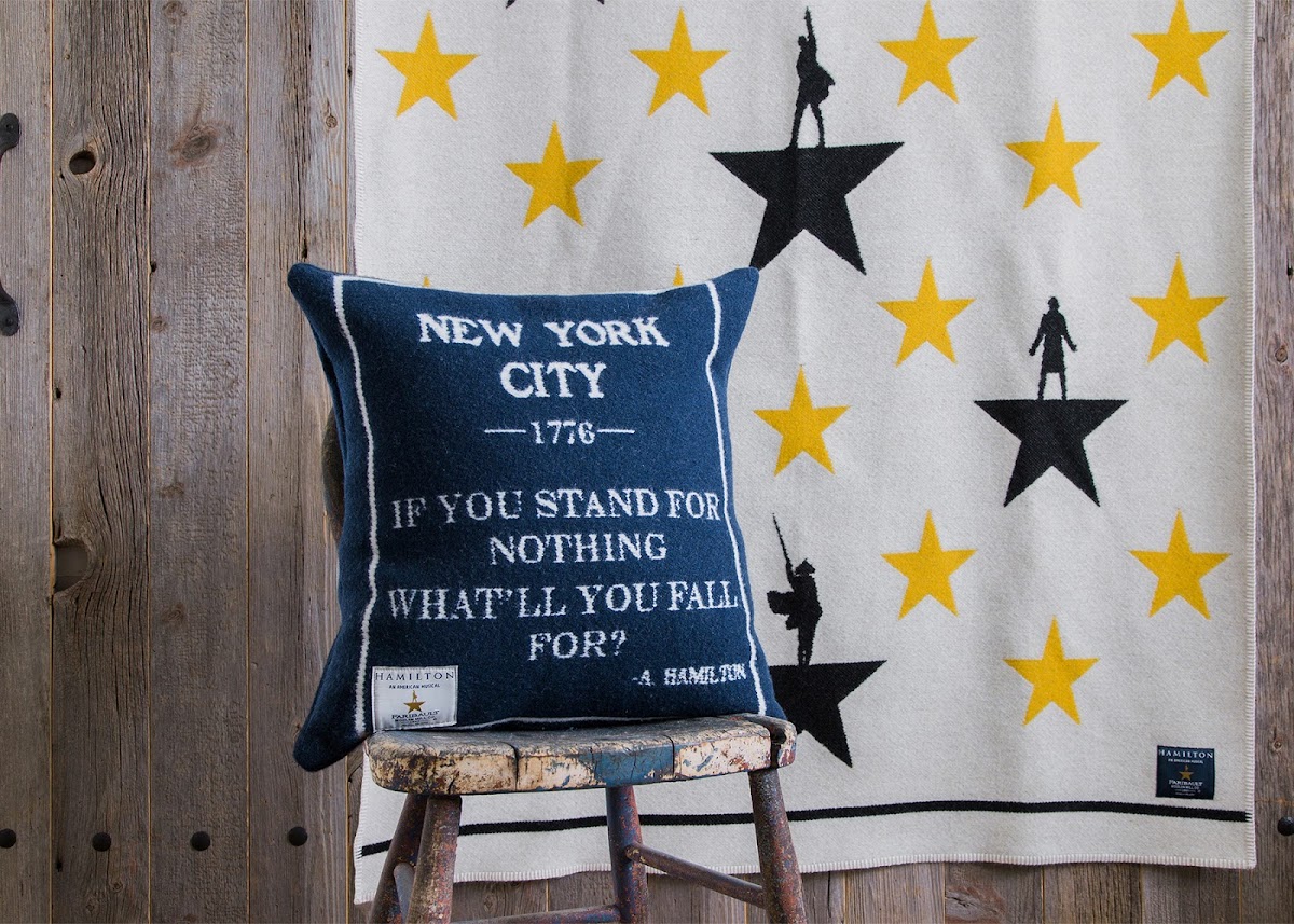 photo of the Hamilton blanket hanging up, decorative pillow on a chair