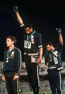 FILe - In this Oct. 16, 1968, file photo, U.S. athletes Tommie Smith, center, and John Carlos stare downward while extending gloved hands skyward during the playing of the Star Spangled Banner after Smith received the gold and Carlos the bronze for the 200 meter run at the Summer Olympic Games in Mexico City. Australian silver medalist Peter Norman is at left. Former Olympic sprint stars and civil activists Tommie Smith and John Carlos became famous when they raised their gloved fists on the medal podium at the 1968 Mexico City Games. On Monday, they return to where they shined on campus at San Jose State and now have a 23-foot statue, helping the university announce it is reinstating its track and field program. (AP Photo/File)