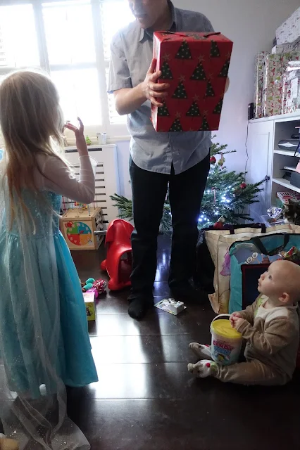 2 children looking up at a man holding a large present