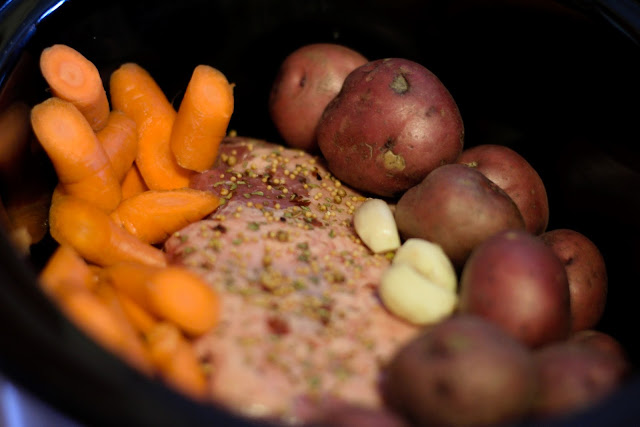 The potatoes, carrots, and garlic being added to the crock pot. 