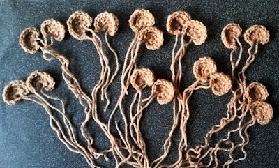 Crocheted ears, each crocheted in a half-circle shape, are arranged in pairs with their loose ends trailing, on a dark background. They are arranged a bit like a bunch of flowers with the ears along the top and the loose ends coming together at the bottom.