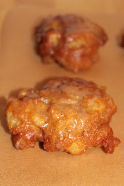 Glazed apple fritters on parchment paper.