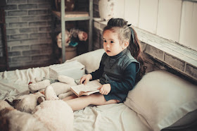 Young girl sitting on her bed, reading a book