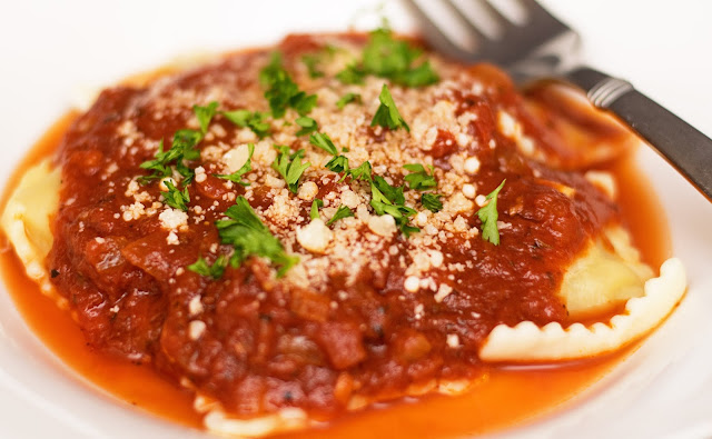 A plate of ravioli with marinara sauce over it.  