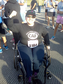 I'm wearing a ballcap that says "Iron Girl," a black shirt that says "Challenged Athletes Foundation," sports pants, running shoes, race number, sitting in my wheelchair