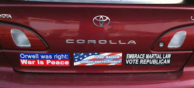 Red car with three bumper stickers, One Nation Under Surveillance; Embrace Martial Law - Vote Republican; and Orwell was right, war is peace