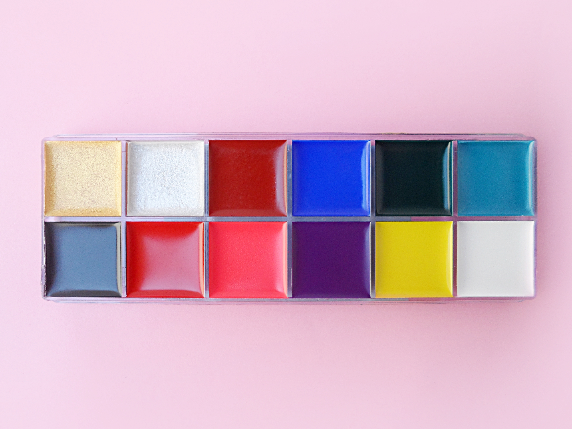 close-up of a 12 color palette with makeup greasepaint on a pink studio background