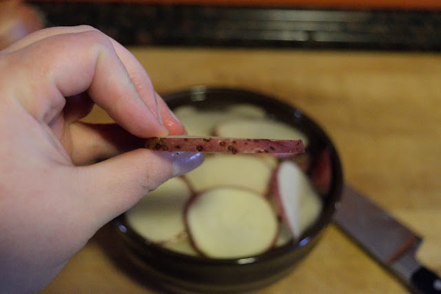A slice of potato being held up to show how thick to cut them.