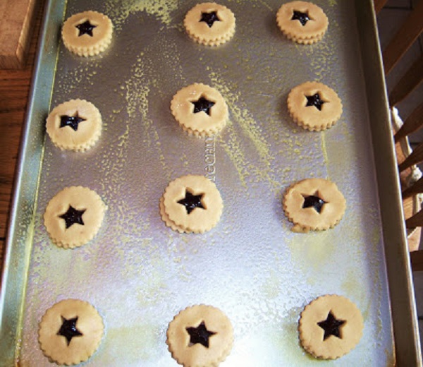 cut out cookies on a cookie sheet ready for baking with raspberry jam filling and a shortbread dough