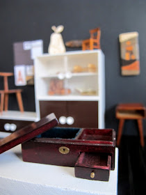 Modern dolls' house miniature plinth in a gallery, showing a wooden case with removable lid and drawer.