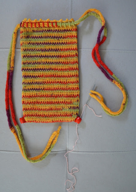 Rectangular crocheted drawstring bag laid flat with a bead stitched to each bottom corner.