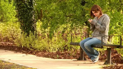 Girl using cellphone on a park bench