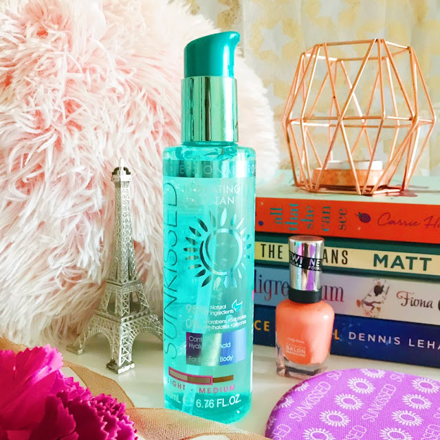 Sunkissed Hydrating Jelly Tan in the centre. Pink fluffy pillow in the background on the left side, stack of books to the right with copper candle holder on top