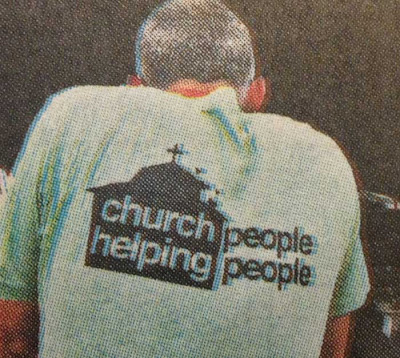 Back of a man wearing a t-shirt that has a black church shape on it with the words Church Helping inside it and then the words People People to the right