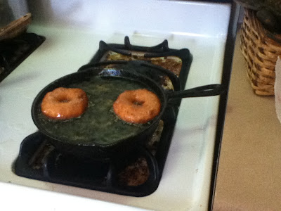 Image shows two doughnuts being fried on the stovetop