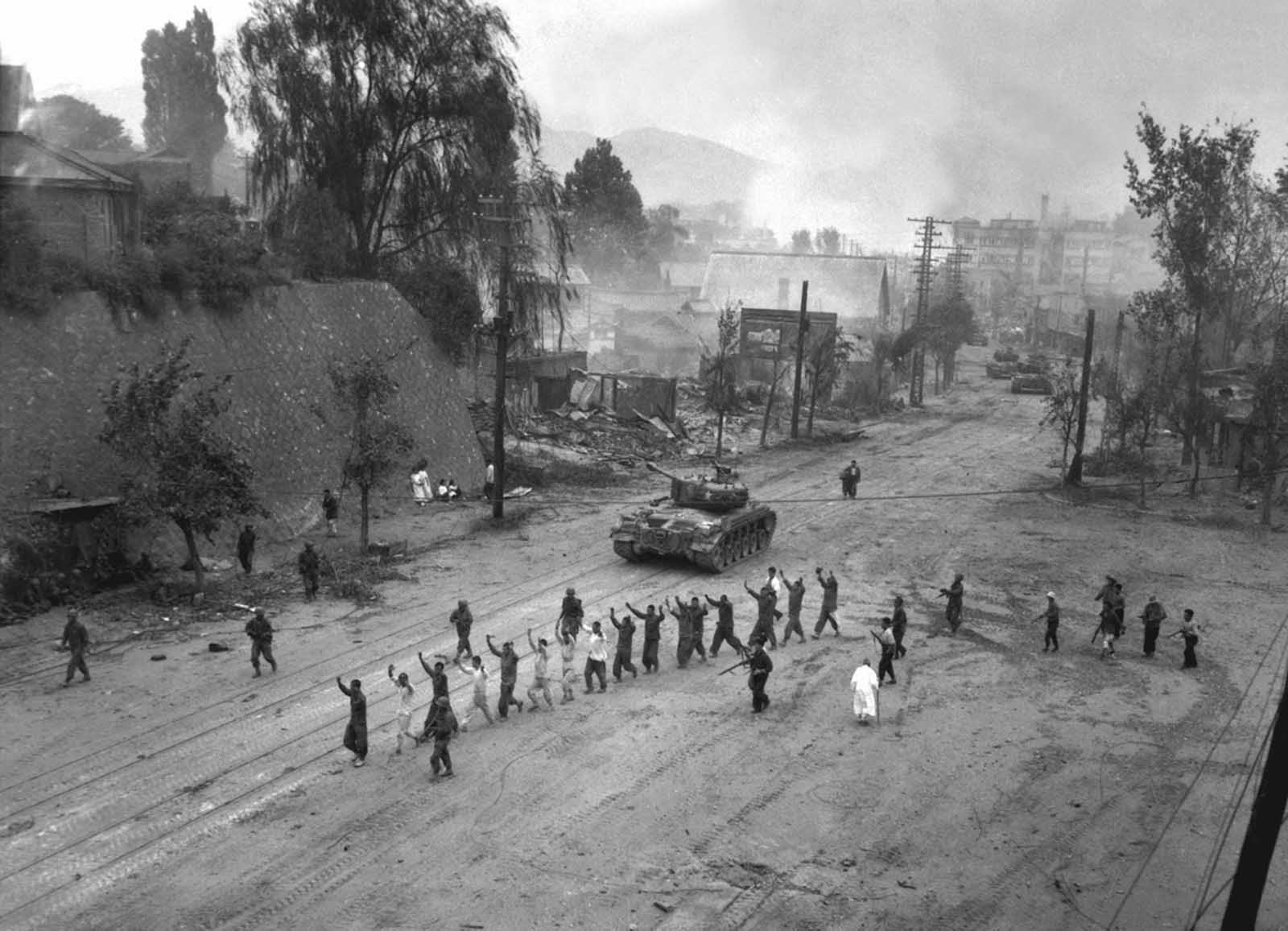 A U.S. Marine tank follows a line of prisoners of war down a village street. September 26, 1950.