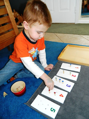 Young son sitting on a blue rug with pegs and a peg card for counting up to five