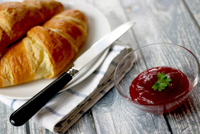 A croissant with a glass bowl of jam.