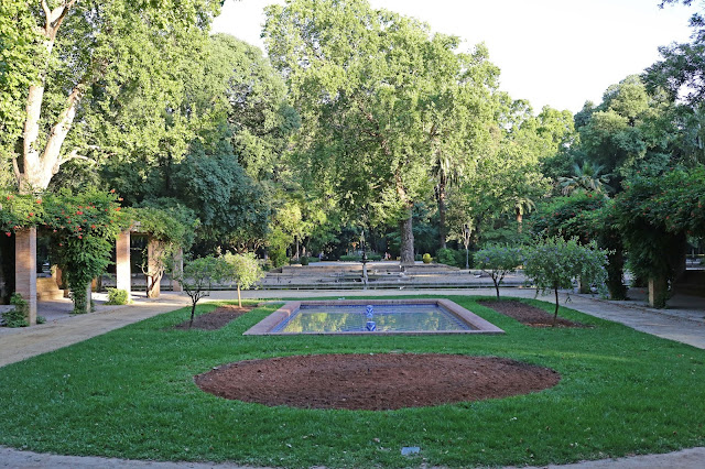plaza en un un parque con un estanque y un monumento rodeado de vegetación.