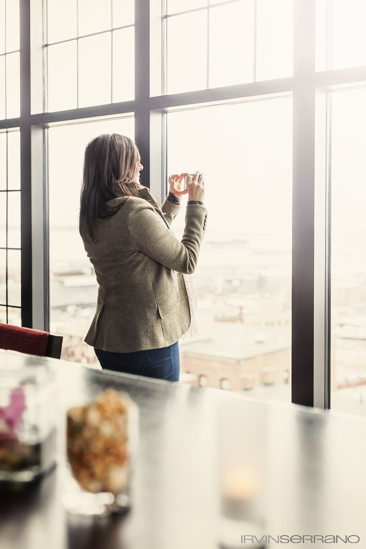 A woman taking a photograph out the windows at Top of the East bar, located on the top floor of the Westin and overlooking the city of Portland, Maine.