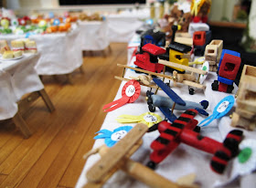 Wooden toys with prize ribbons on a stall in a one-twelfth scale scene of a CWI wartime fundraising fete in a hall.