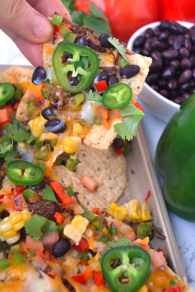Loaded Sheet Pan Nachos come together in 15 minutes and are packed with sauteed black beans, bell peppers, melted cheese, jalapenos, corn, cilantro, tomatoes and shredded steak! www.nutritionistreviews.com